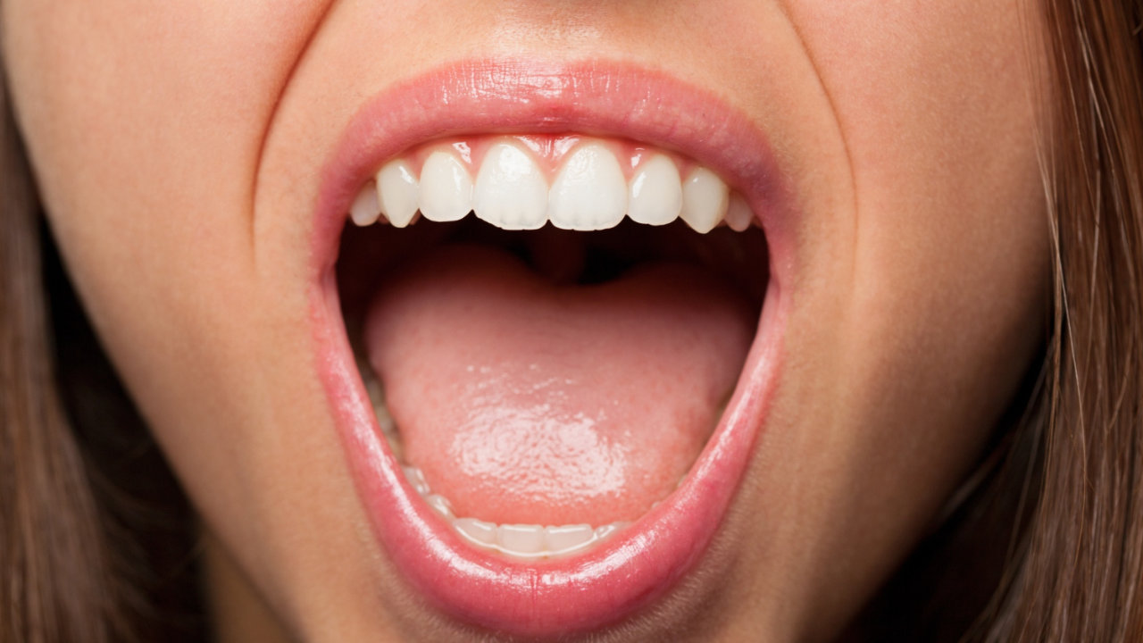 Boca de una persona en primer plano, se observa la lengua, dientes y saliva.
